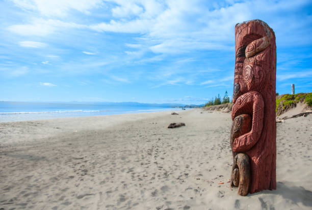 sandy beach with tall carved Māori pou