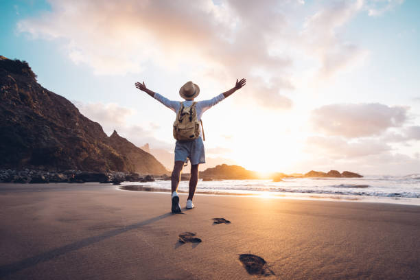 Traveler standing on beach at sunrise with arms raised